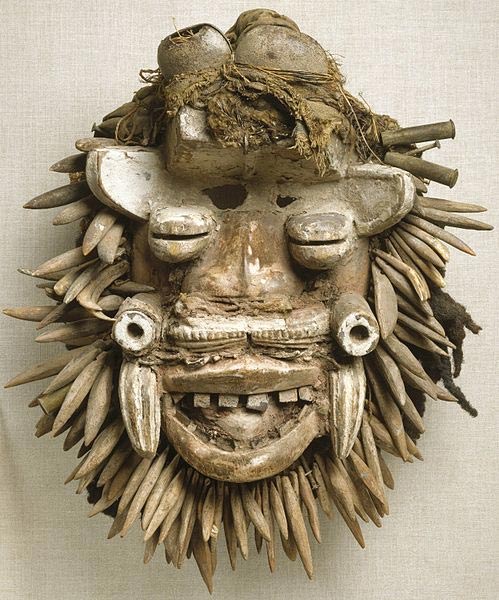 This African face mask, which appears to represent a bush spirit, contains animal and human composits. This mask combines many diverse materials to create an image of power. Multiple eyes, warthog tusks, large teeth, and other power symbols such as rifle casings and a beard of authentic and wooden leopard's teeth form a fierce countenance that frightens away negative forces. 